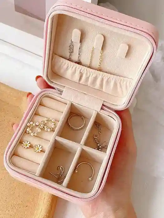 Pink jewelry box with compartments filled with earrings and a ring, held by a hand.