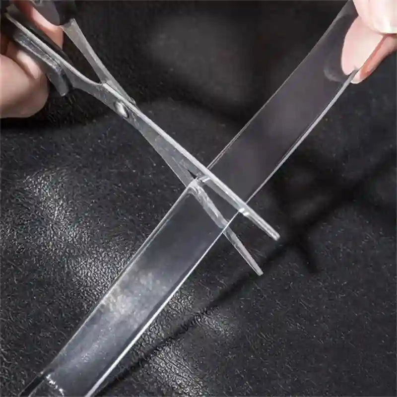 Person cutting clear plastic sheet with scissors on a dark textured surface