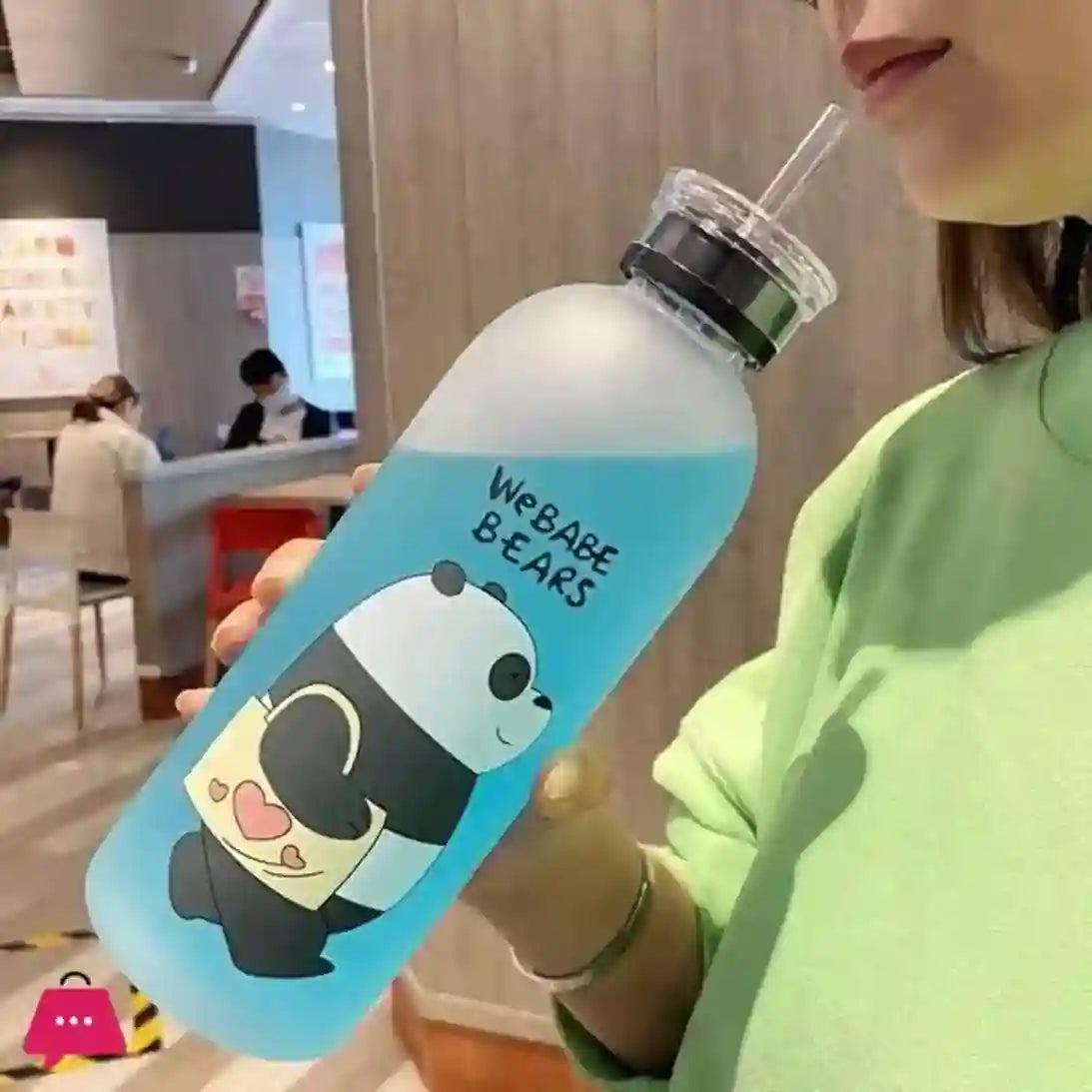 Person holding a blue water bottle with a panda design and text indoors.