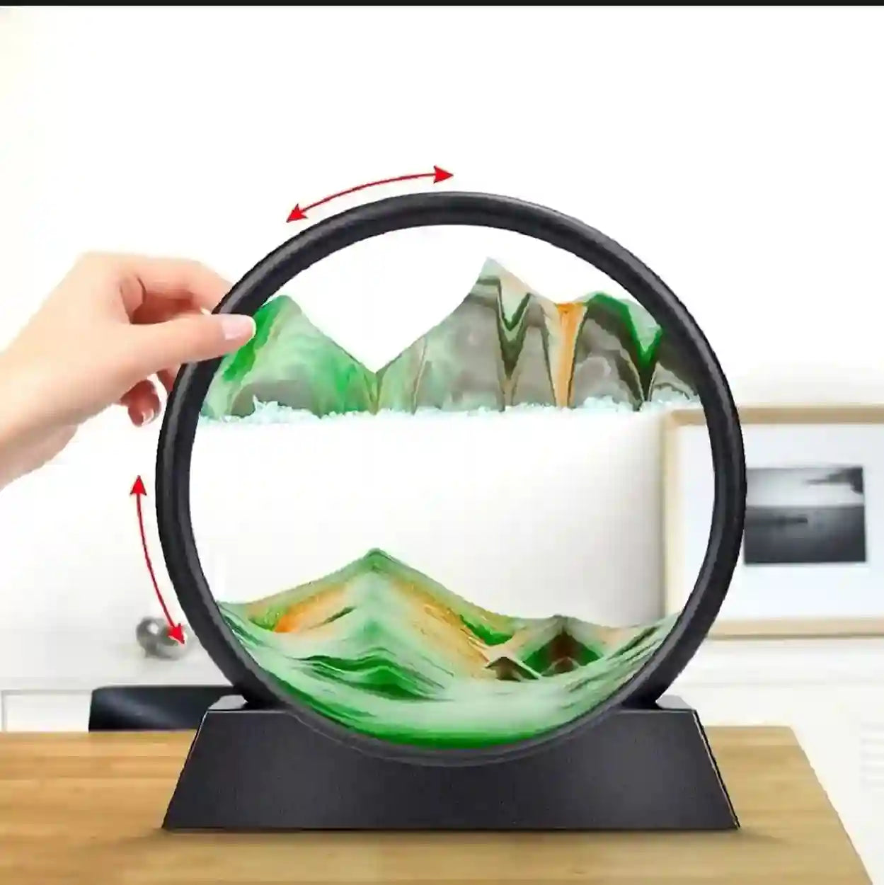 Circular object with mountain and cloud design, held by a hand on a wooden surface.
