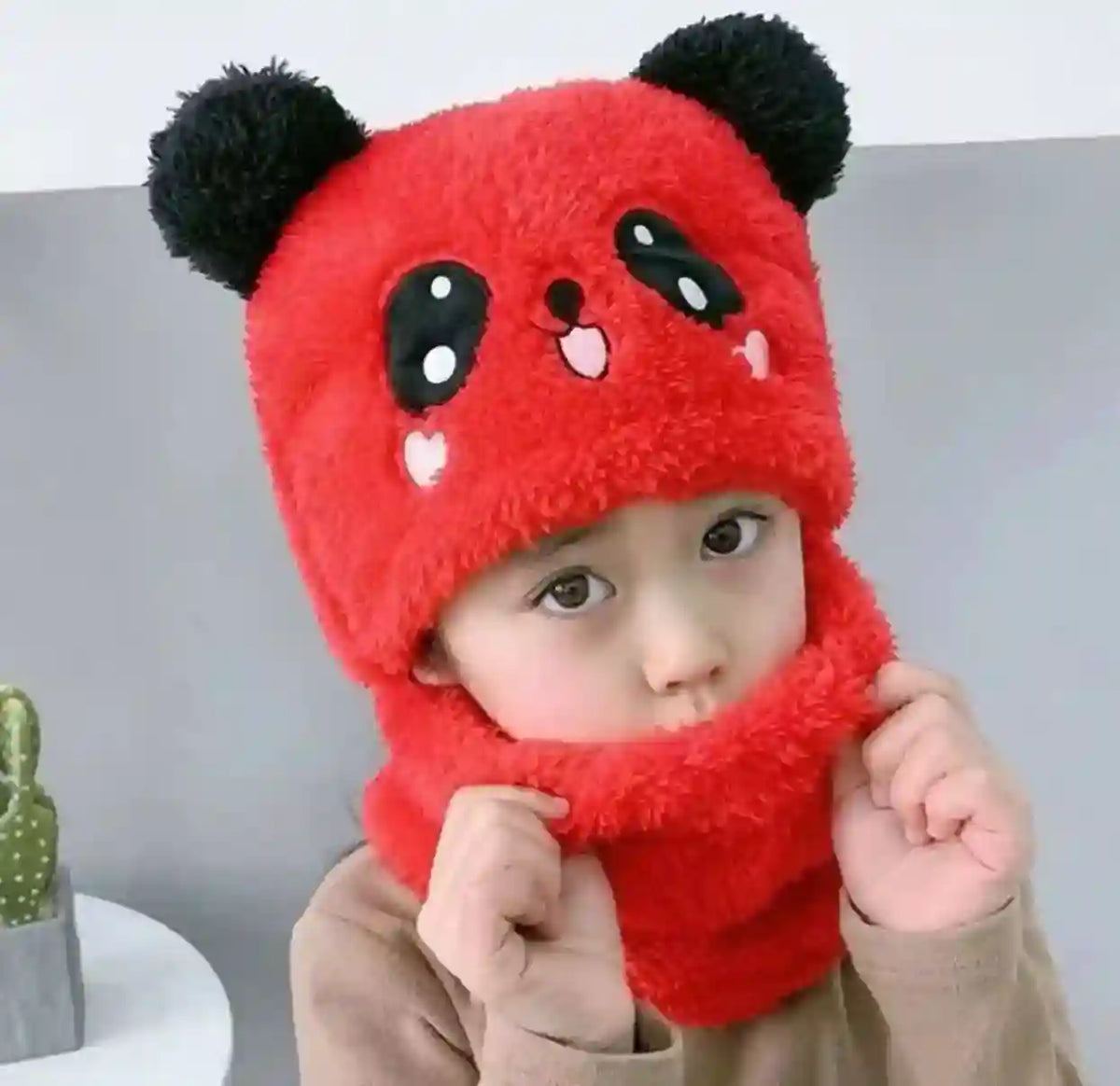 Child wearing a red panda-themed hat and scarf on a plain background