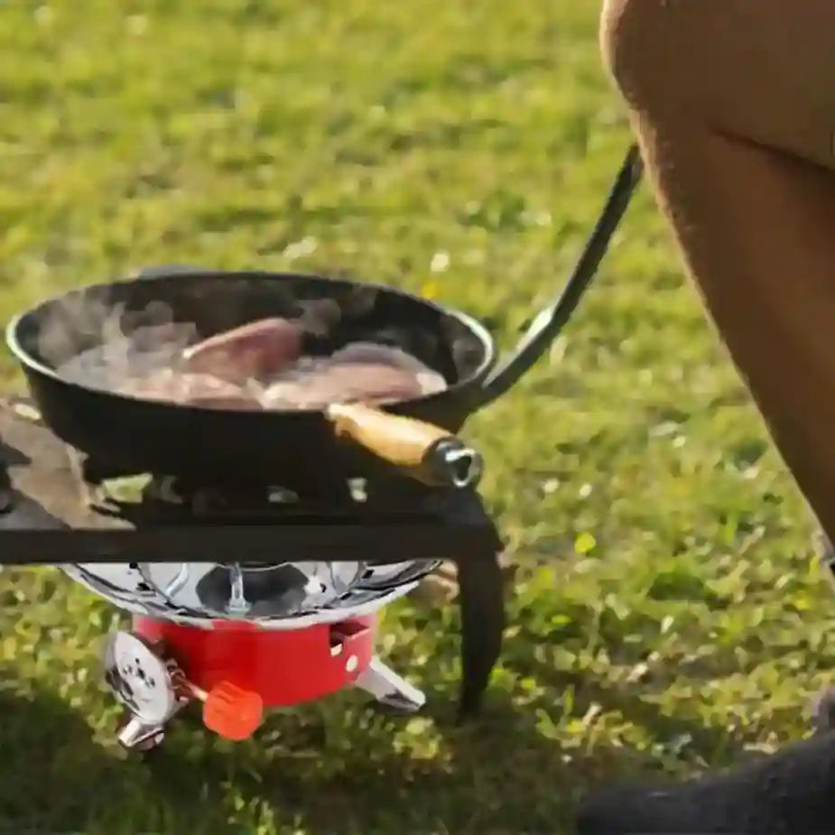 Person cooking on a portable stove with a frying pan outdoors