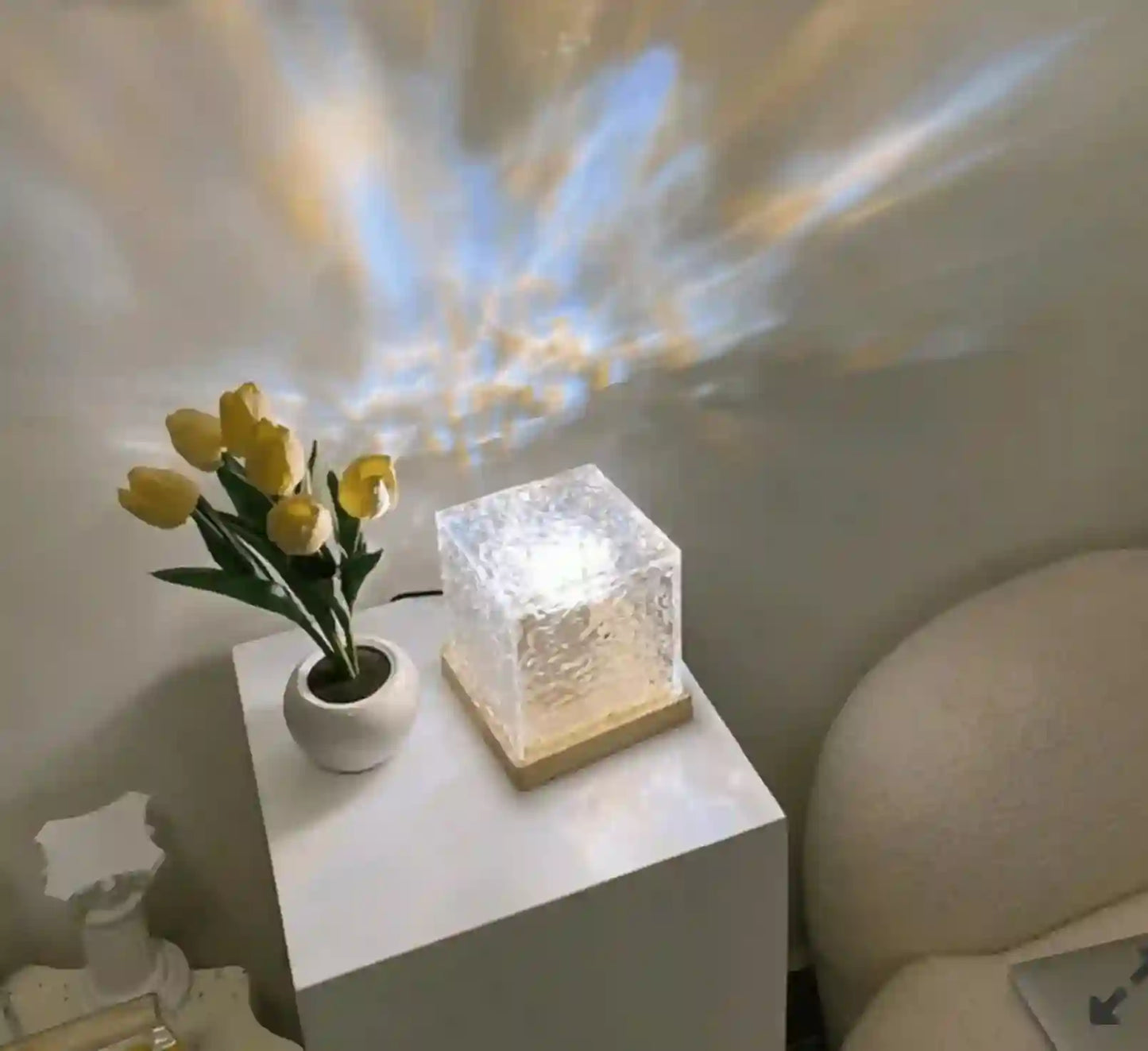 Small table with a vase of yellow tulips and a decorative light cube on a white surface.