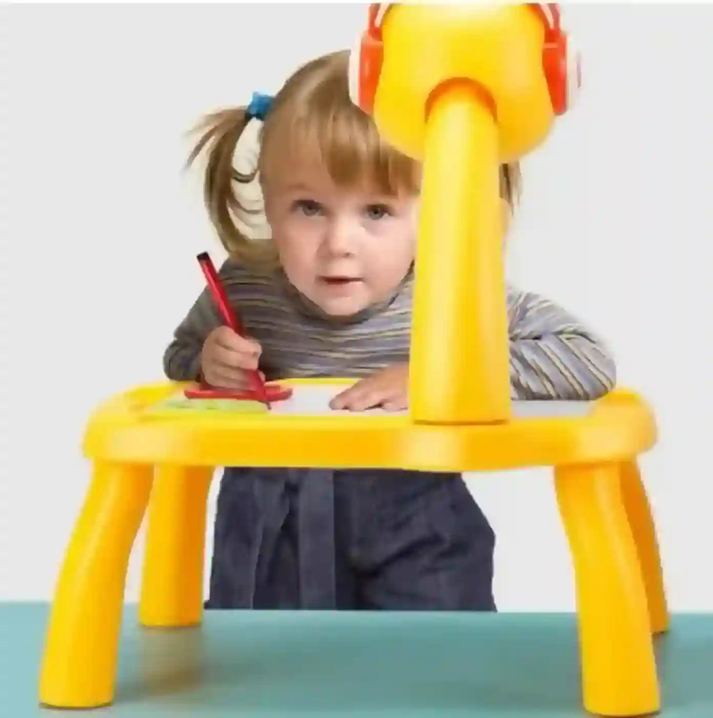 Child using a yellow children's desk with a red pen on a light gray background
