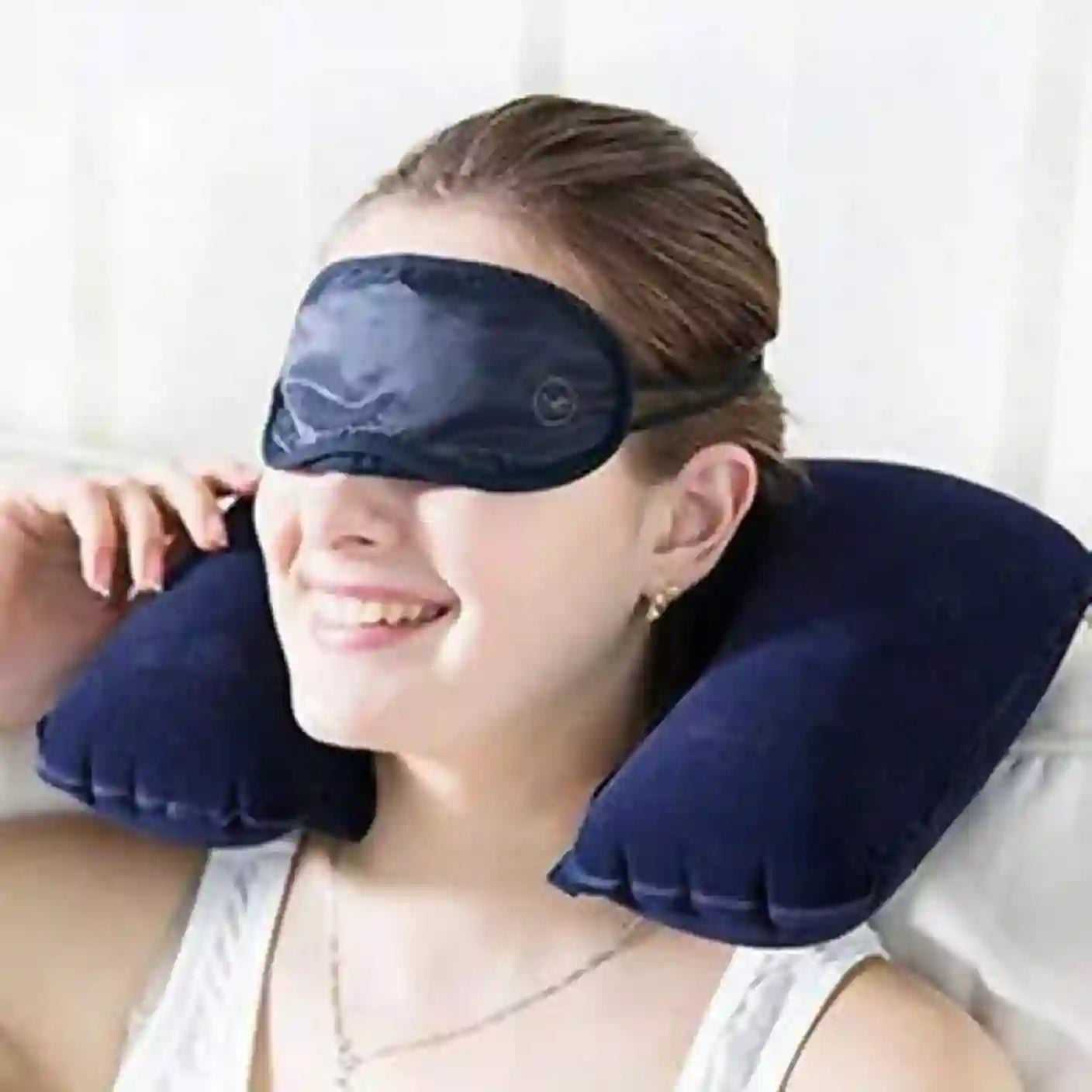 Person using a navy blue eye mask and neck pillow on a white background