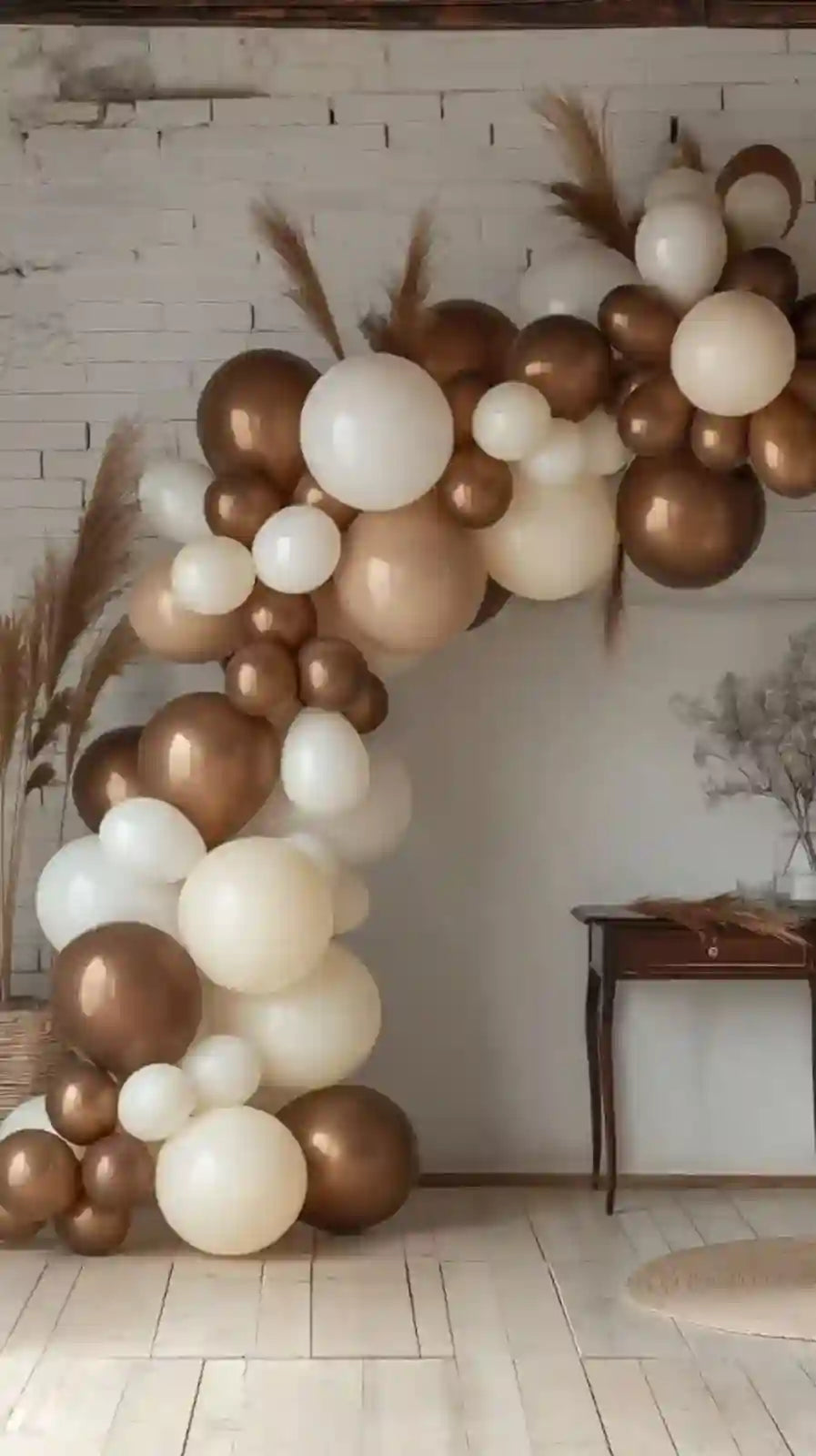 Balloon arch with gold, white, and brown balloons against a white wall.