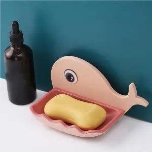 Pink whale-shaped soap dish with a bar of soap on a white surface against a teal wall.