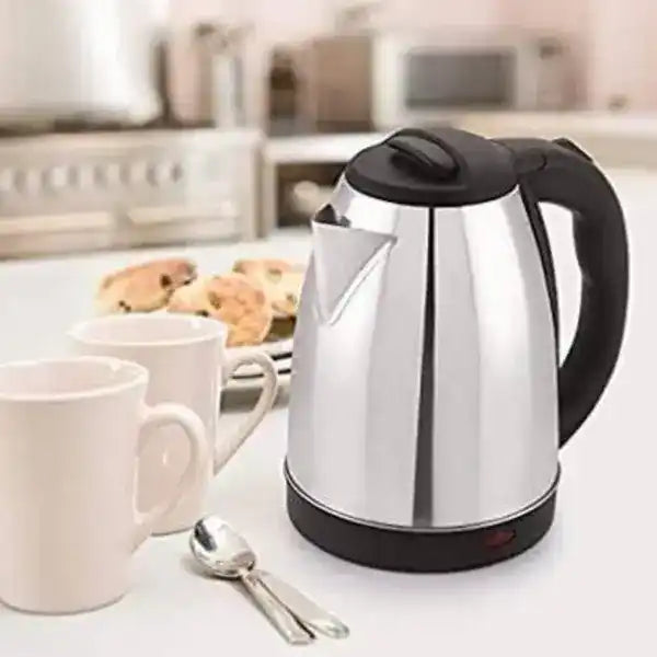 Stainless steel electric kettle on a kitchen counter with mugs and pastries in the background