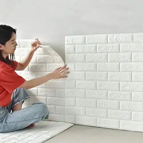 Person installing white brick-patterned wall panels on a wall.