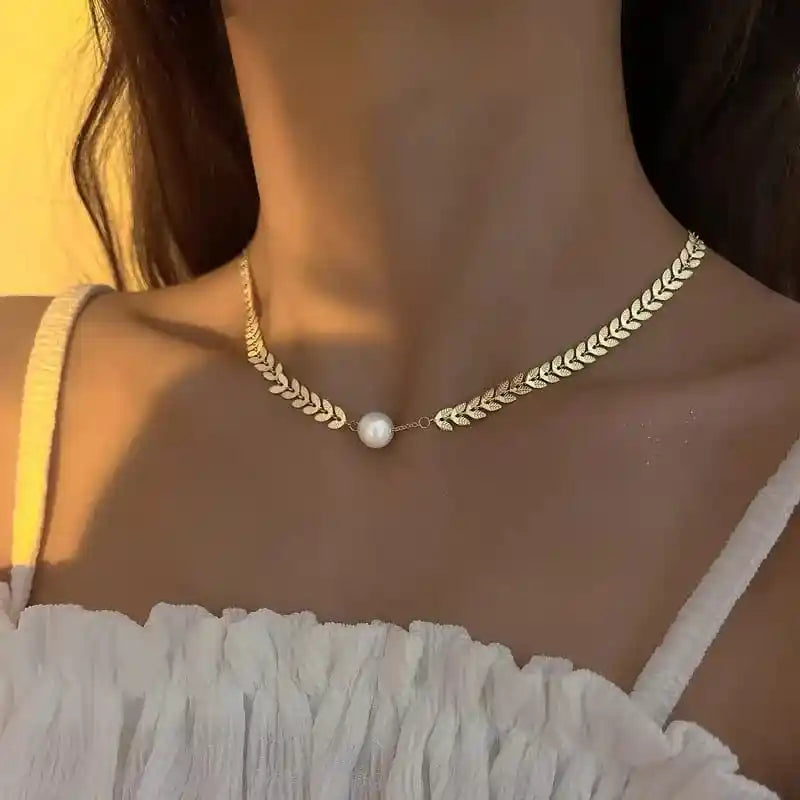 Gold necklace with a pearl pendant worn by a person against a neutral background