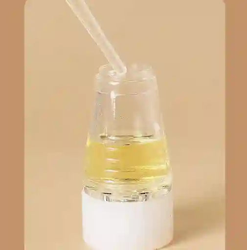Clear glass bottle with yellow liquid and a straw on a beige background
