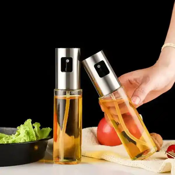Two oil sprayers with a hand holding one, set against a kitchen backdrop.