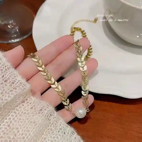 Gold bracelet with a pearl on a hand, with a cup and saucer in the background.