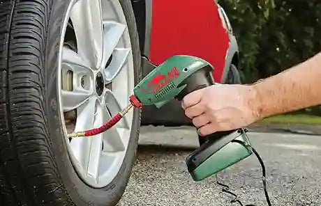 Person using a green tire inflator to inflate a car tire.
