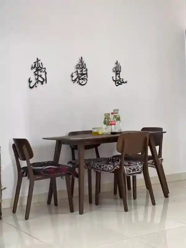 Dining area with wooden table and chairs against a white wall with Arabic calligraphy.