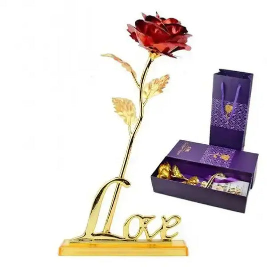 Red rose with gold stem on a 'LOVE' stand next to a purple gift box with chocolates.