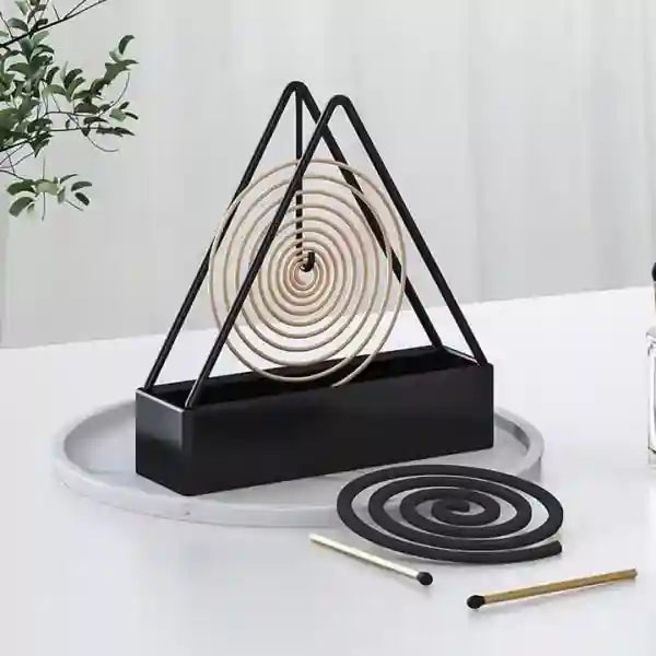 Black triangular incense holder with coiled incense on a white surface.