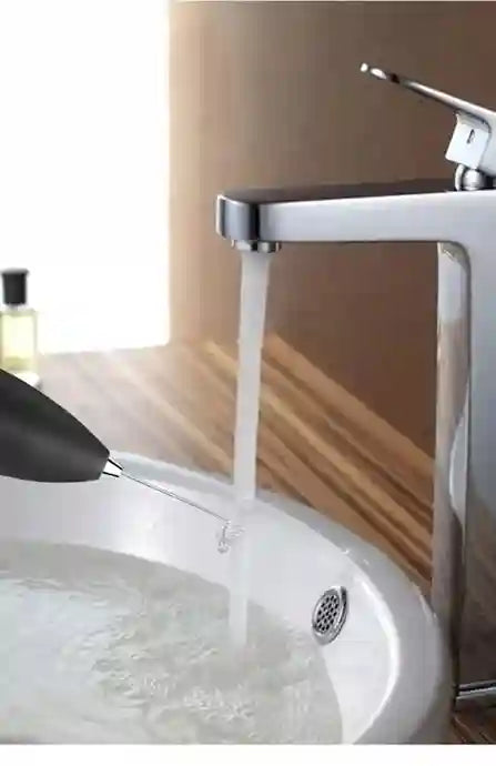 Chrome faucet with water flowing into a sink against a neutral background