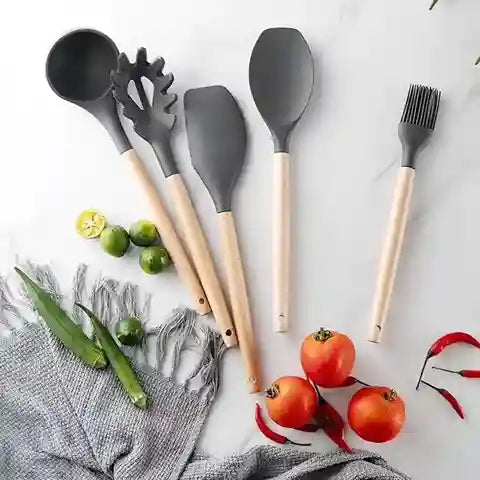 Set of gray kitchen utensils with wooden handles on a white surface with vegetables.