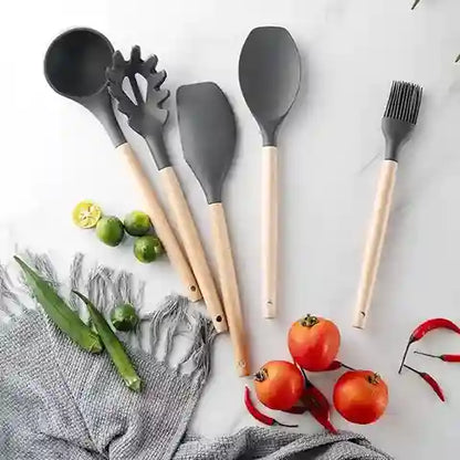 Set of gray kitchen utensils with wooden handles on a white surface with vegetables.