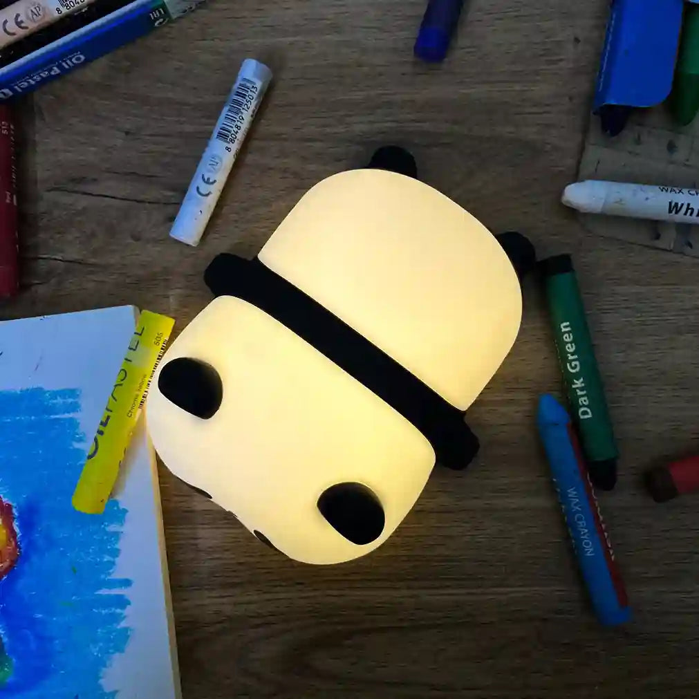 Panda-shaped night light on a wooden surface with markers and books around