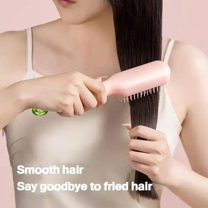 Person brushing long hair with a pink brush against a light pink background