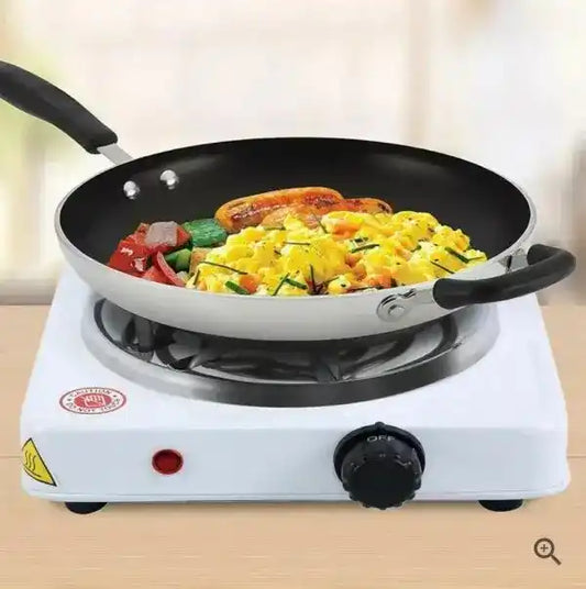 Single burner stove with a frying pan containing eggs, sausages, and vegetables on a light background.