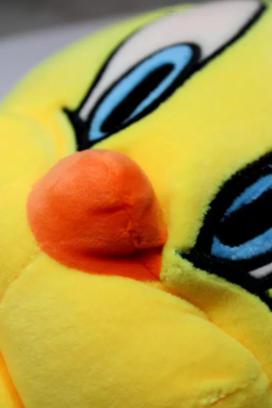 Close-up of a yellow plush toy with a red nose and black eyes.
