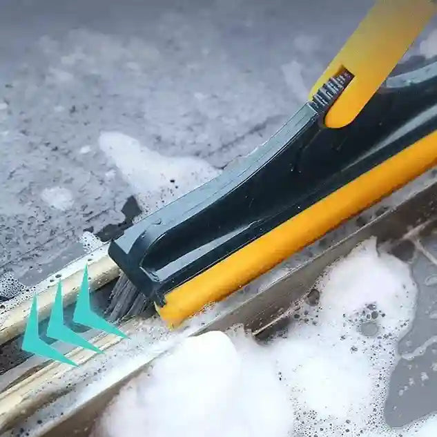 Cleaning tool with a yellow handle and black blade cleaning a surface with soap suds.