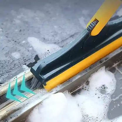 Cleaning tool with a yellow handle and black blade cleaning a surface with soap suds.