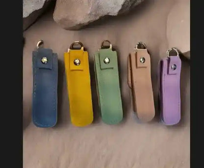 Five leather keychains in blue, yellow, green, brown, and purple on a stone surface.