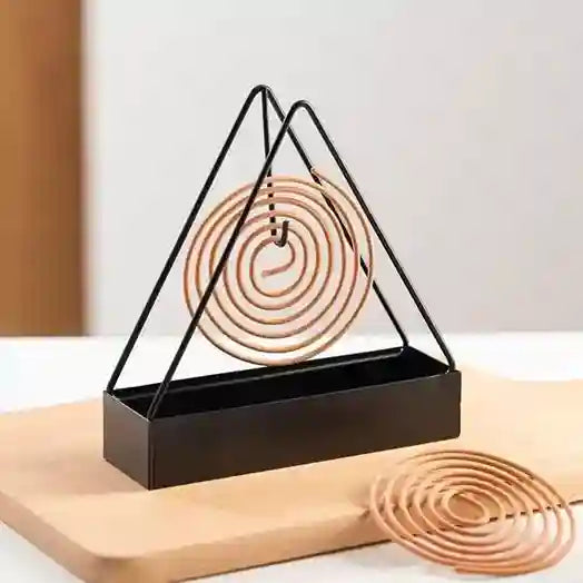 Triangular metal holder with incense coils on a light background