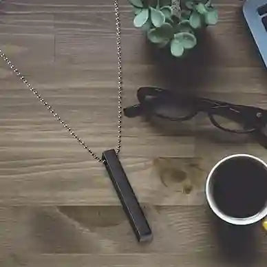 Necklace with a bar pendant on a wooden surface with a plant and cup in the background