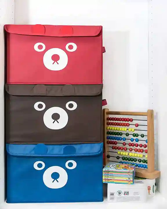 Three bear-shaped storage bins in red, brown, and blue with an abacus and books in the background.