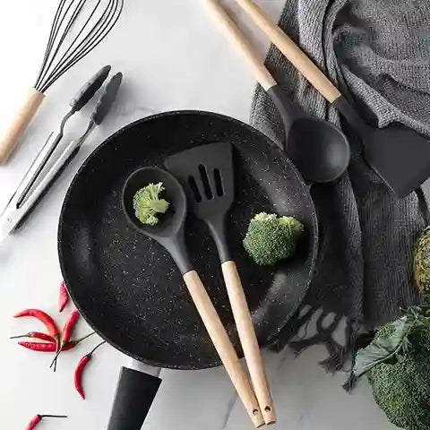 Black frying pan with kitchen utensils and vegetables on a light surface