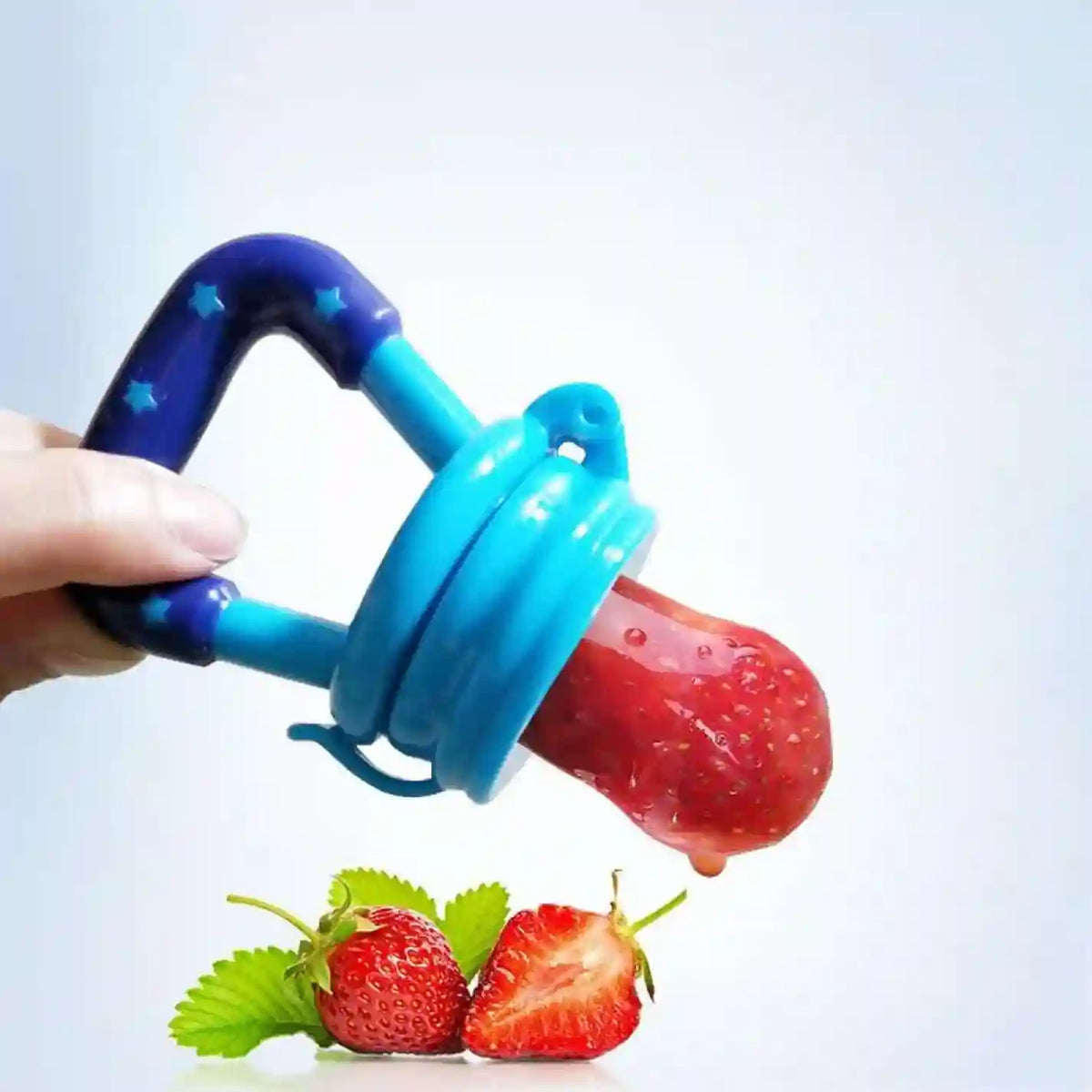 Blue and purple fruit feeder with a strawberry inside, held by a hand on a light blue background.