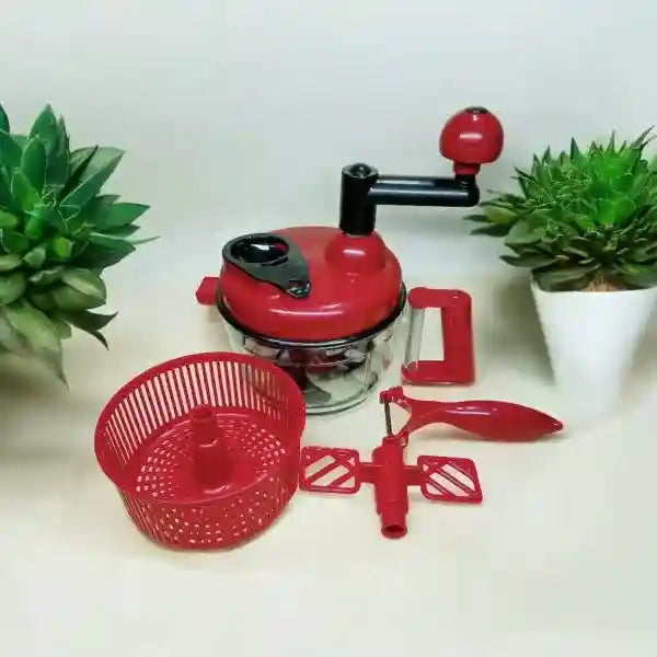 Red manual juicer with components on a white surface with green plants.