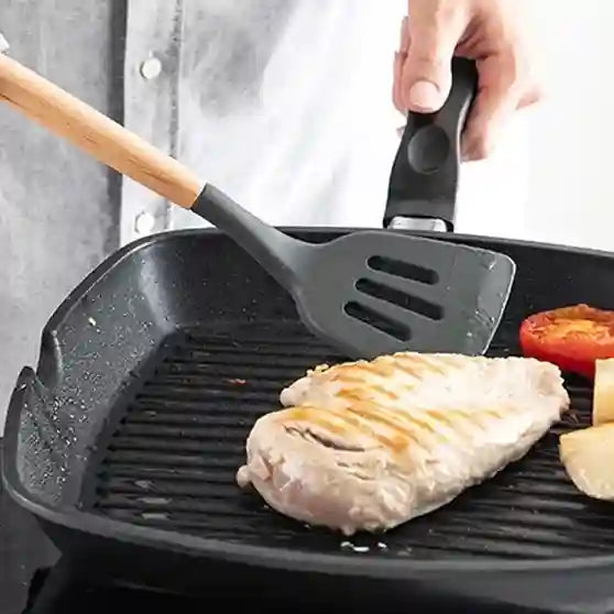 Person cooking chicken breast in a grill pan with a spatula