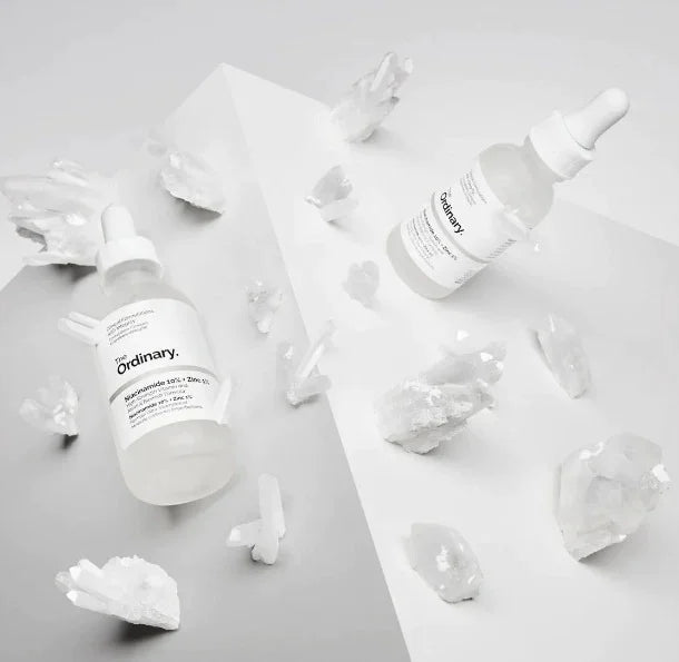 Two 'The Ordinary' skincare bottles on a light gray background with ice cubes.