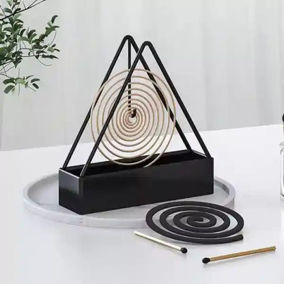 Black triangular incense holder with coiled incense on a white surface.