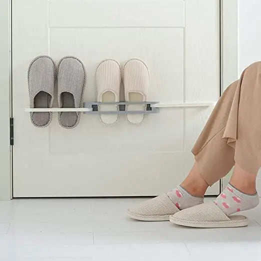 Person wearing light gray slippers with a shelf holding additional pairs on a white tiled floor.