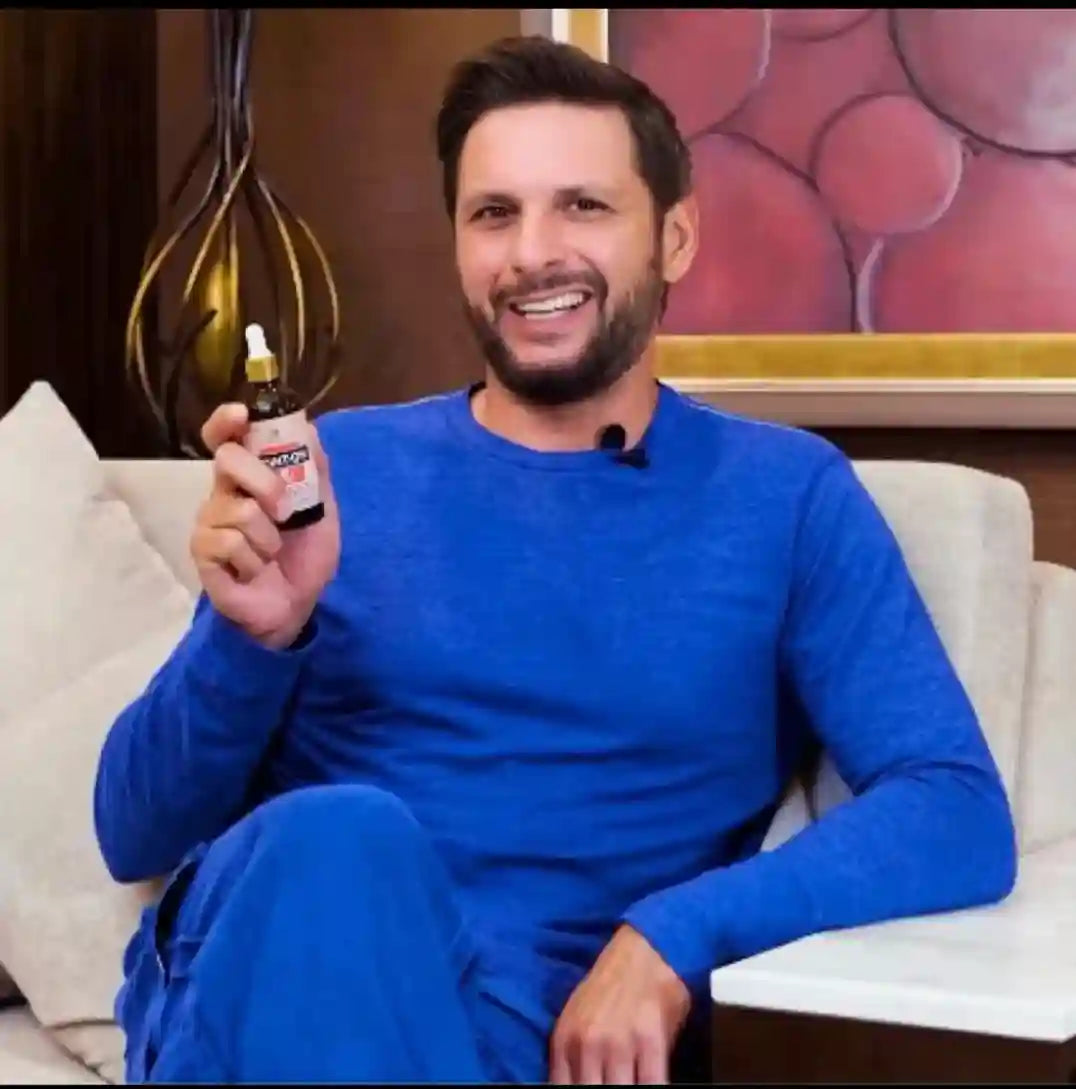 Man in blue outfit holding a bottle, sitting on a couch with a decorative background