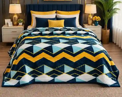 A bed dressed in a geometric patterned quilt featuring navy blue, yellow, light blue, and white zigzag and triangle motifs, styled in a modern bedroom with matching pillows, bedside tables, lamps, and a plant.