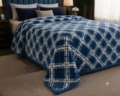 A plush blue and white plaid blanket draped over a bed in a bedroom setting, with matching pillows and a dark blue upholstered headboard visible in the background.
