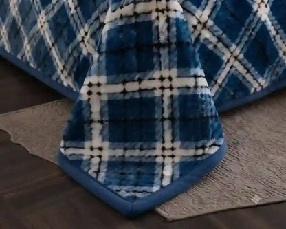 A close-up of a blue and white plaid fleece blanket draped over a bed, showing its soft texture and quilted pattern.