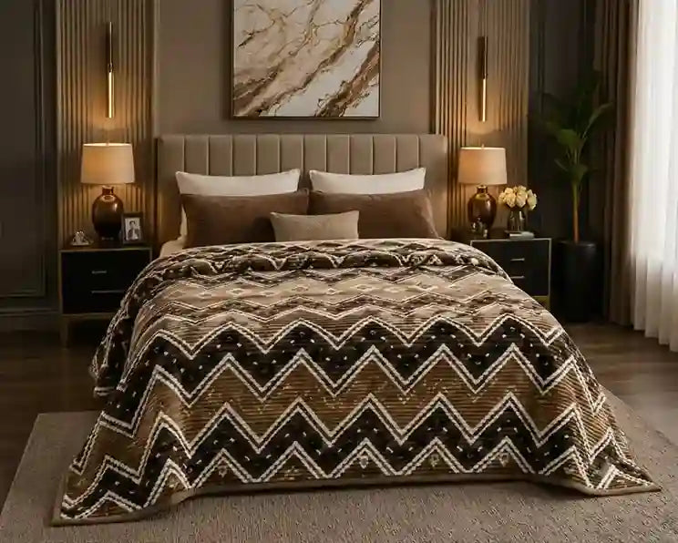 A bed dressed in a brown, beige, and black chevron-patterned comforter set, styled in a modern, warm-toned bedroom with matching pillows, bedside tables, lamps, and wall art.