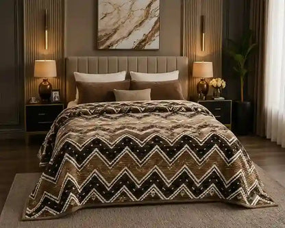 A bed dressed in a brown, beige, and black chevron-patterned comforter set, styled in a modern, warm-toned bedroom with matching pillows, bedside tables, lamps, and wall art.