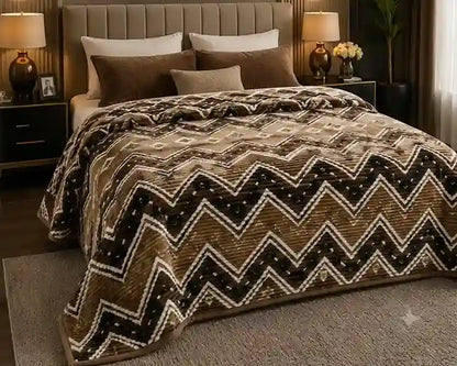 A plush bedspread with a brown, beige, and white chevron pattern, styled on a bed in a modern bedroom setting.