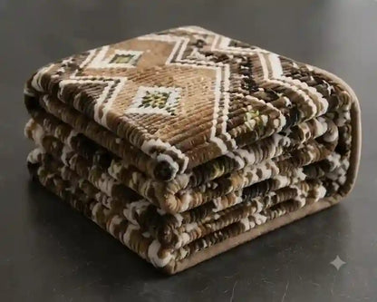 A stack of folded woven prayer rugs with a geometric pattern in brown, beige, and white, set against a dark gray background.