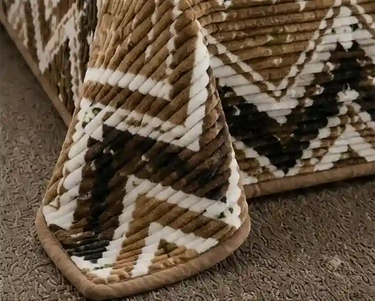 A close-up of a textured bath mat with a geometric chevron pattern in brown, beige, and white, resting on a gray carpet.